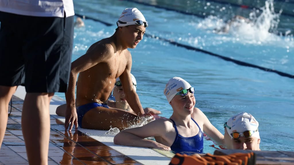 Coach at the poolside talking with a few swimmers at the pool wall